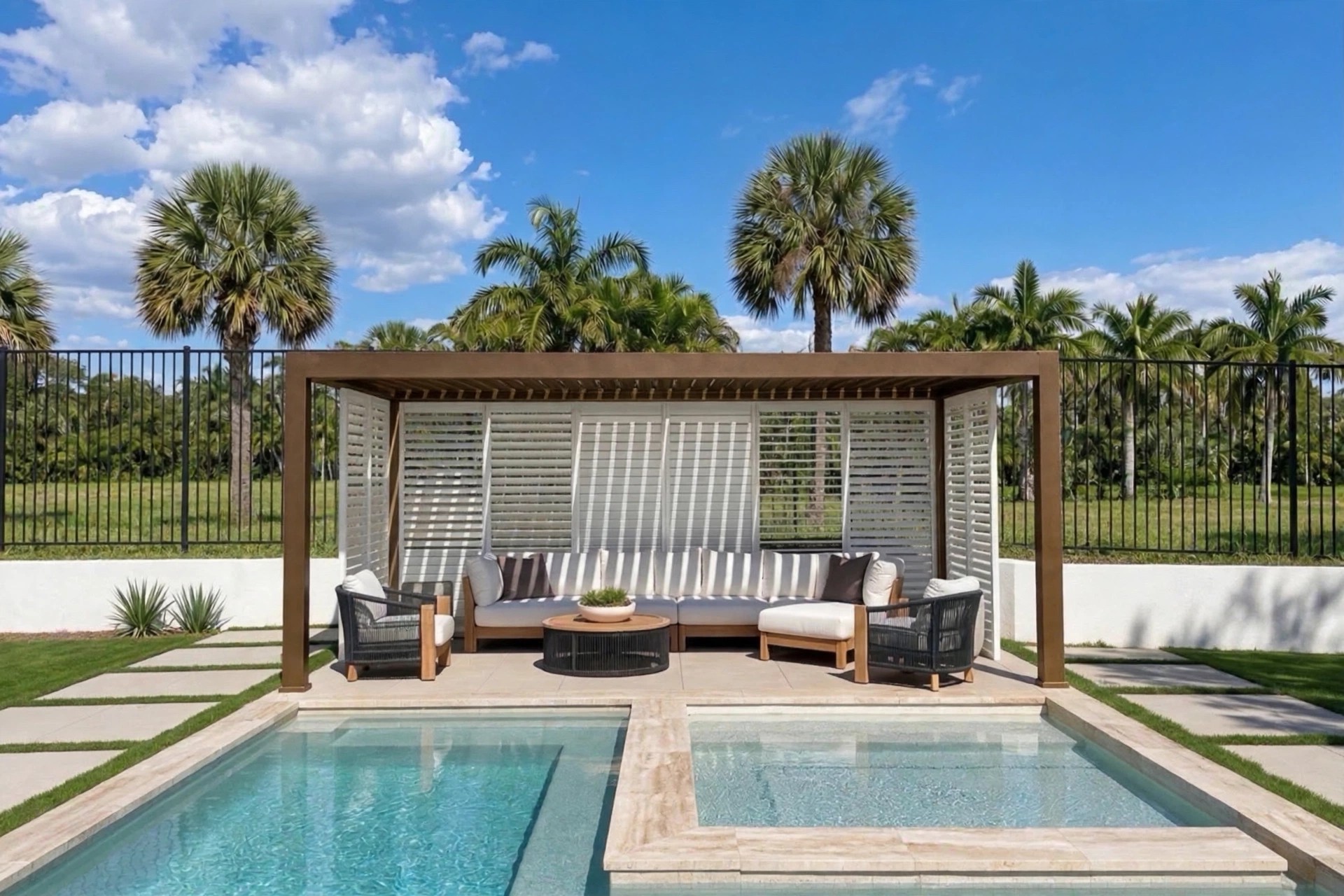 Motorized louvered pergola in a bronze frame with white shutters and a sectional by a Florida pool, palm trees behind the fence