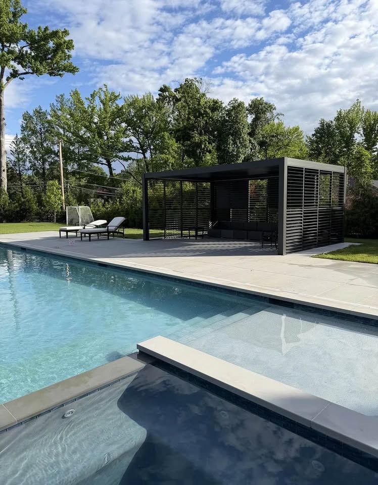 Dark pergola with slat walls on all sides, set beside a long swimming pool