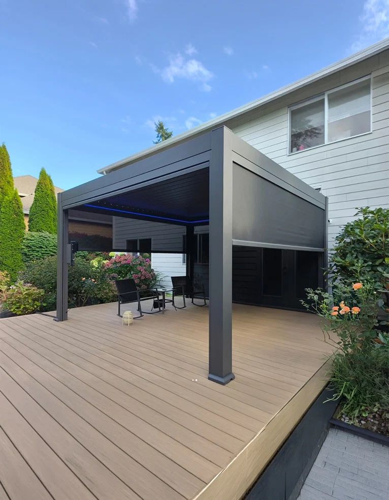 Dark pergola on a wooden deck with its drop screen down and blue LED light in the beams