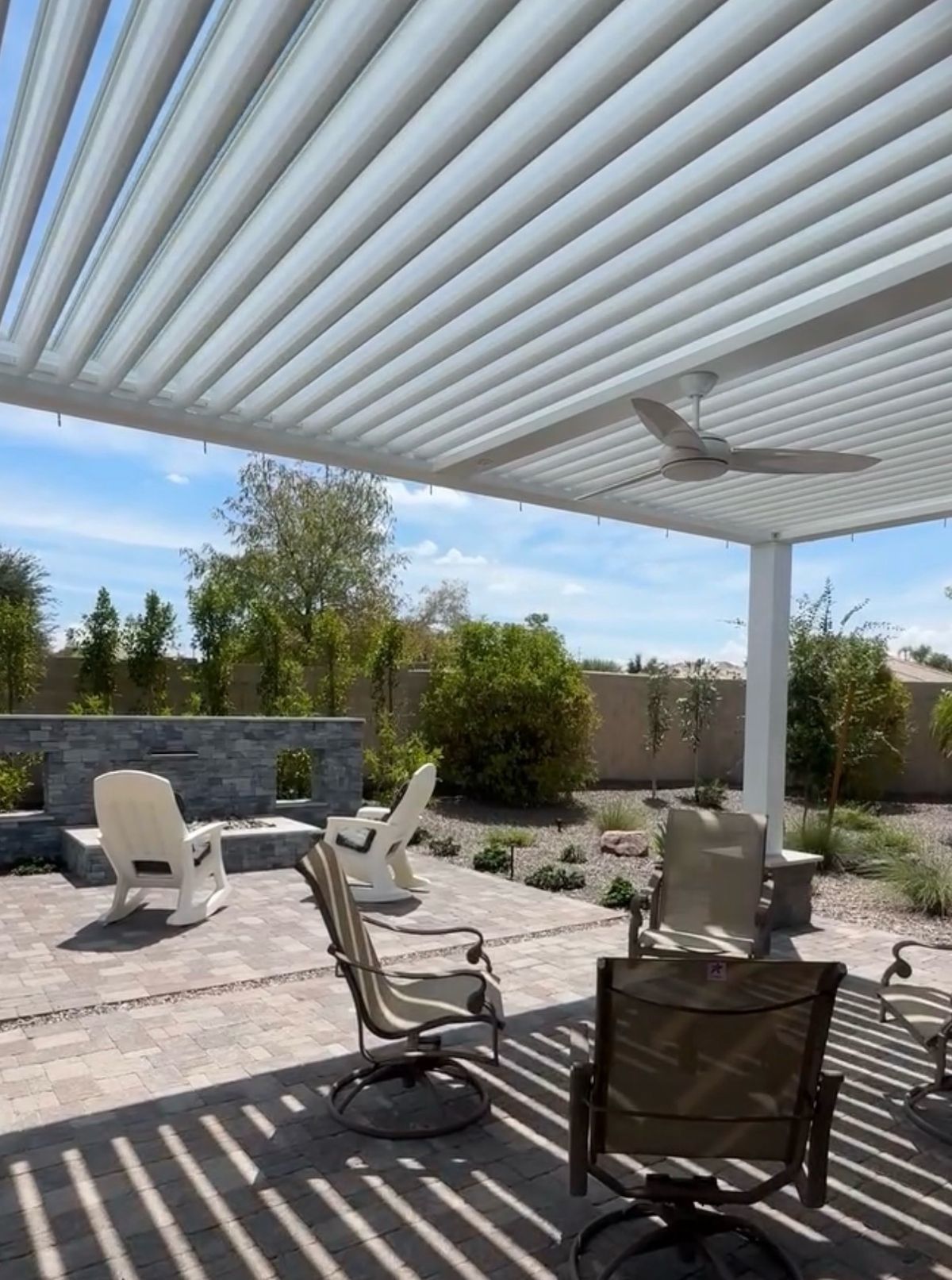 White pergola with louvers open and a ceiling fan, patio chairs in striped shade