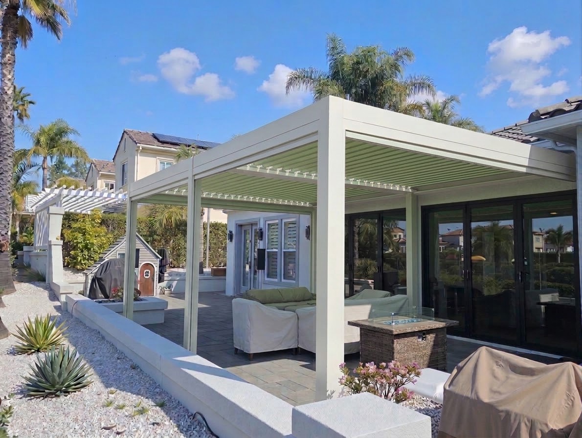 Finished custom pergola in a white frame with green louvers, attached to a house, palms beside it