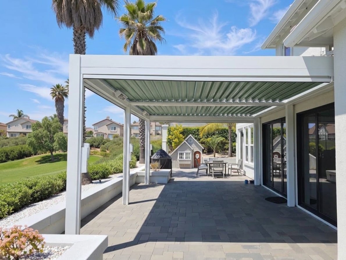 White frame motorized pergola with sage green louvers running the length of a house patio, designed around the home and yard
